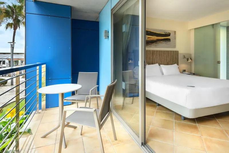 Une chambre lumineuse s'ouvre sur une terrasse avec table et chaises.
