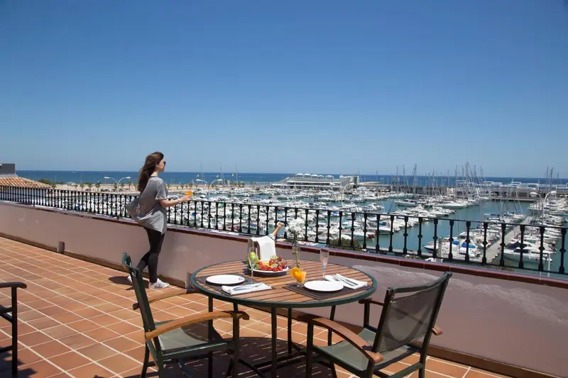 Une personne se tient sur une terrasse avec vue sur un port de plaisance ensoleillé.