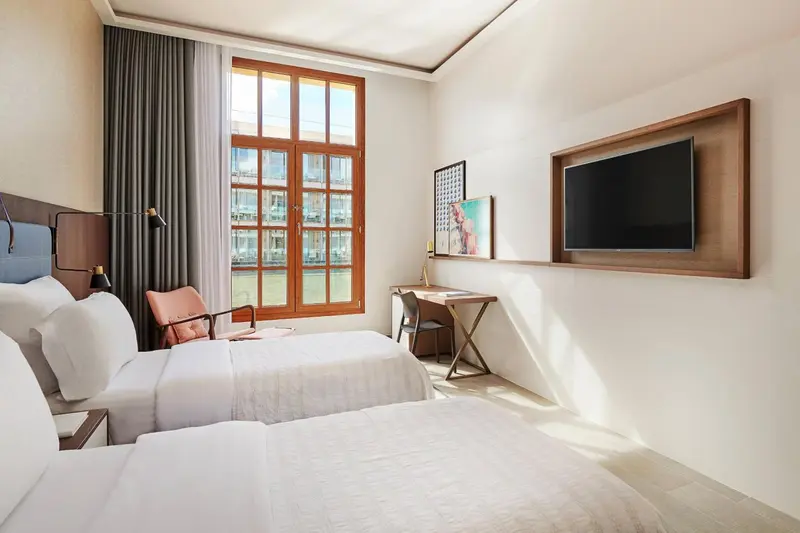 Une chambre lumineuse avec un lit double et un bureau près d'une fenêtre.