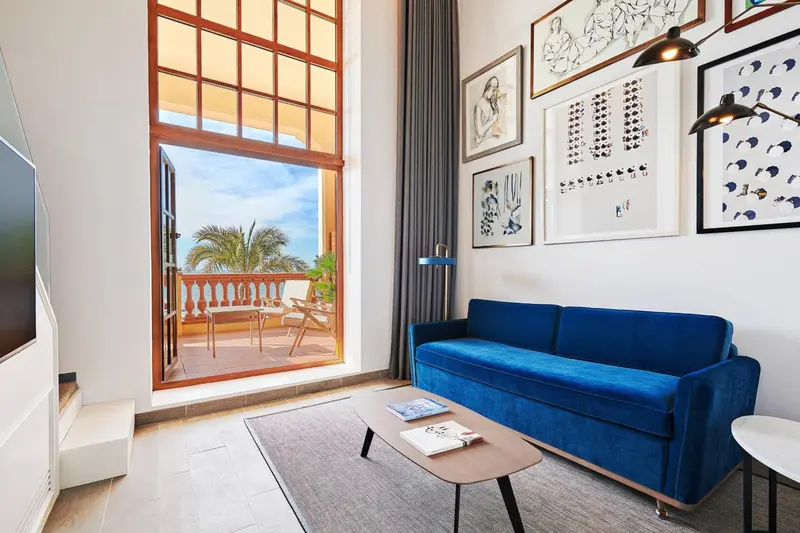 Un salon bleu vif s'ouvre sur un balcon avec vue sur la végétation.