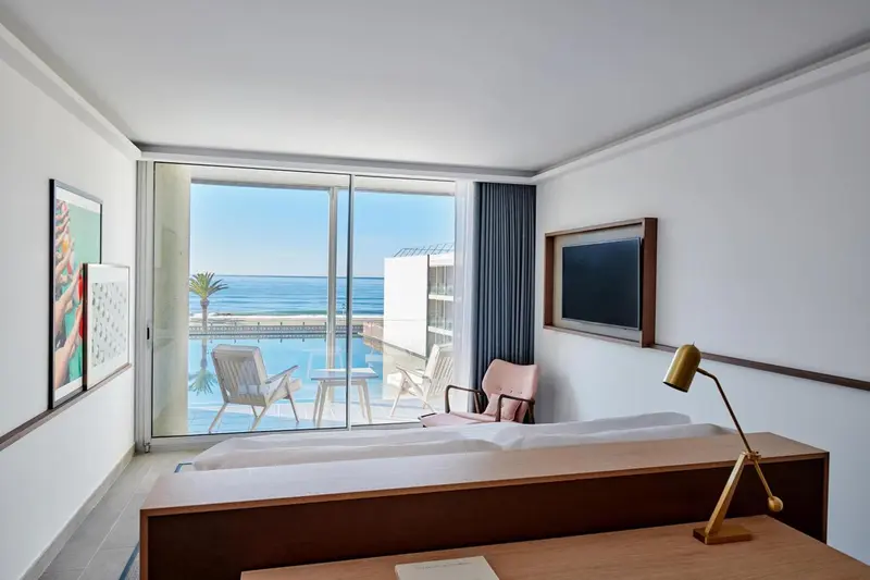 Chambre lumineuse avec vue sur la mer depuis un balcon.