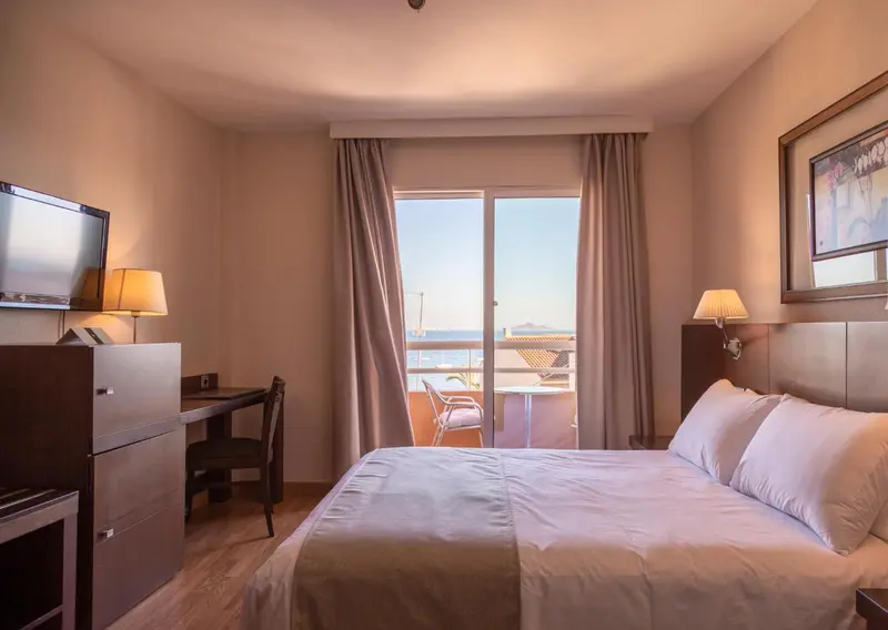 Une chambre lumineuse avec un lit et un bureau donnant sur une vue mer.