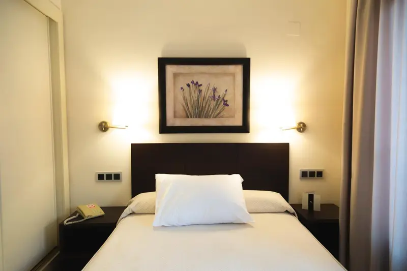 Un lit simple avec une tête de lit sombre et des lampes murales.