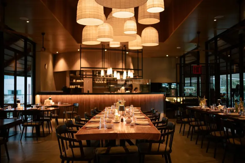 Une salle de restaurant lumineuse avec de longues tables en bois et des suspensions décoratives.