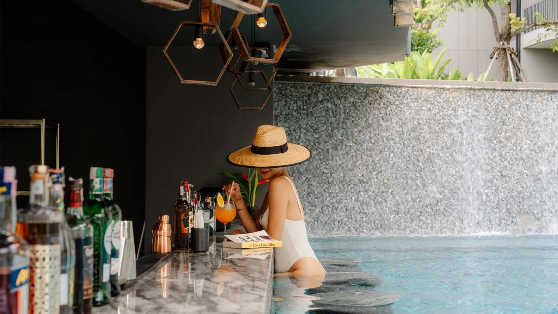 Une femme assise au bar déguste une boisson colorée près d'une piscine.
