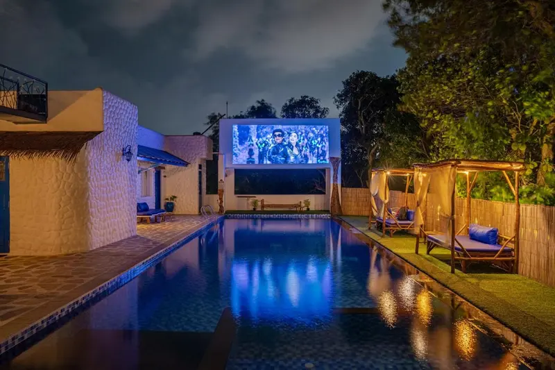 Une piscine illuminée avec un écran de cinéma en plein air et des transats.
