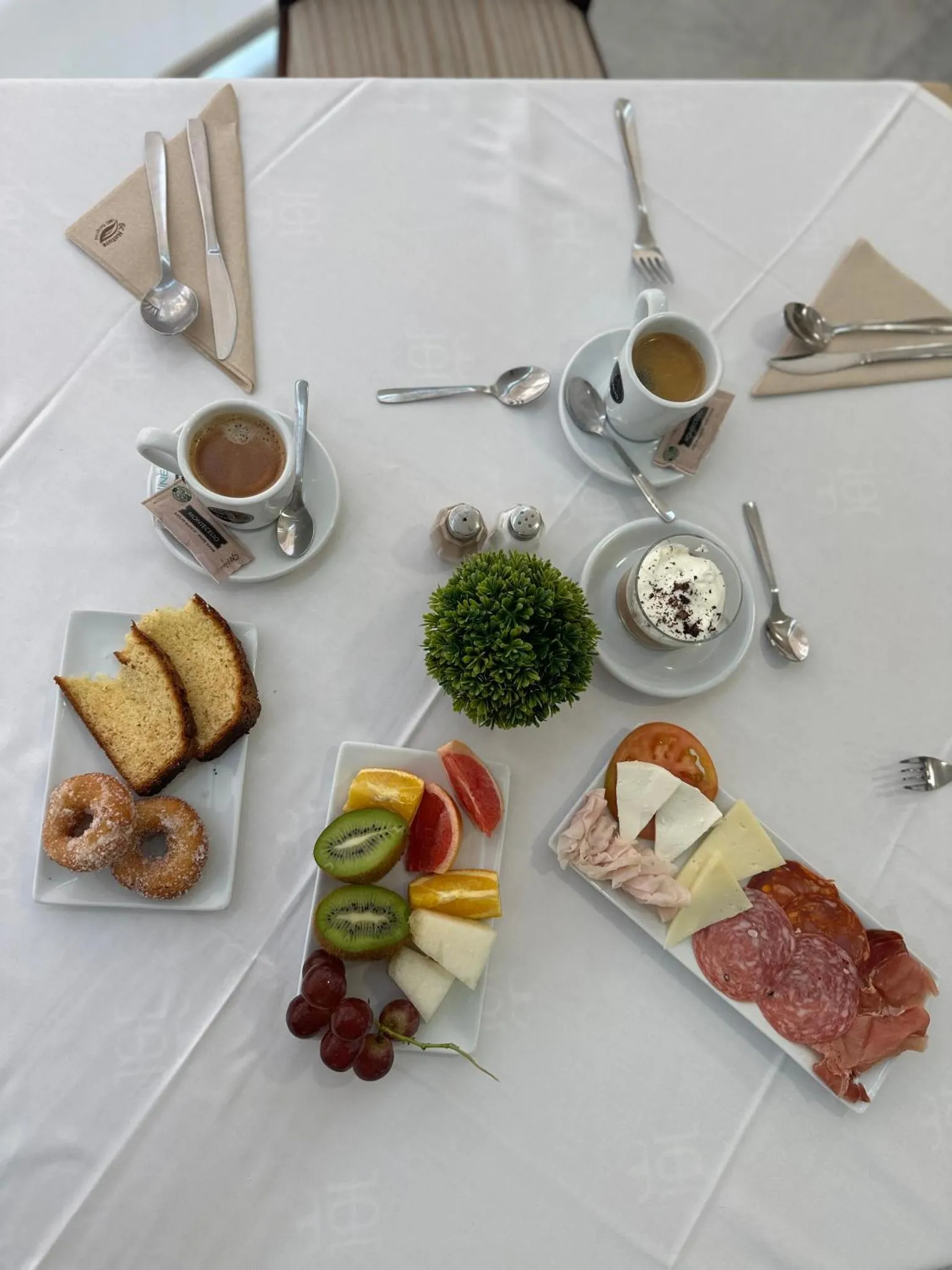 Une table dressée pour le petit-déjeuner avec des viennoiseries, des fruits et des boissons.
