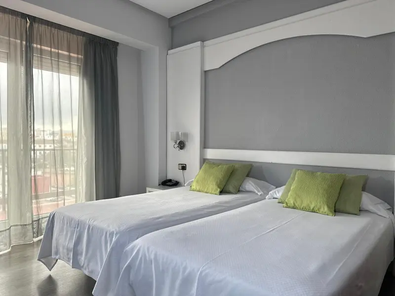 Une chambre lumineuse avec deux lits simples et des coussins verts.
