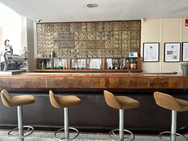Un comptoir de bar en bois avec des tabourets est présenté dans un espace lumineux.