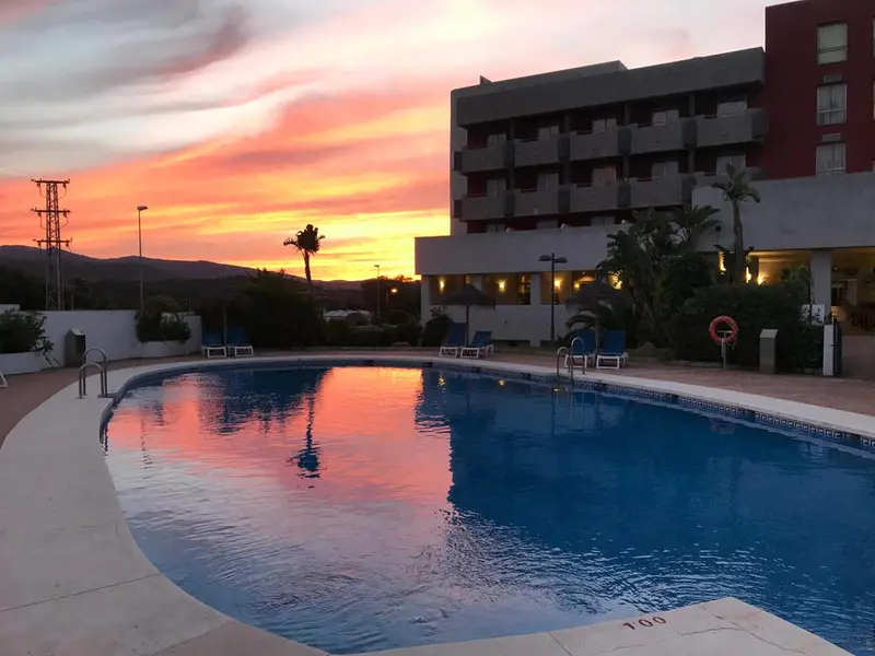 Une piscine reflète les couleurs d'un coucher de soleil sur un paysage montagneux.