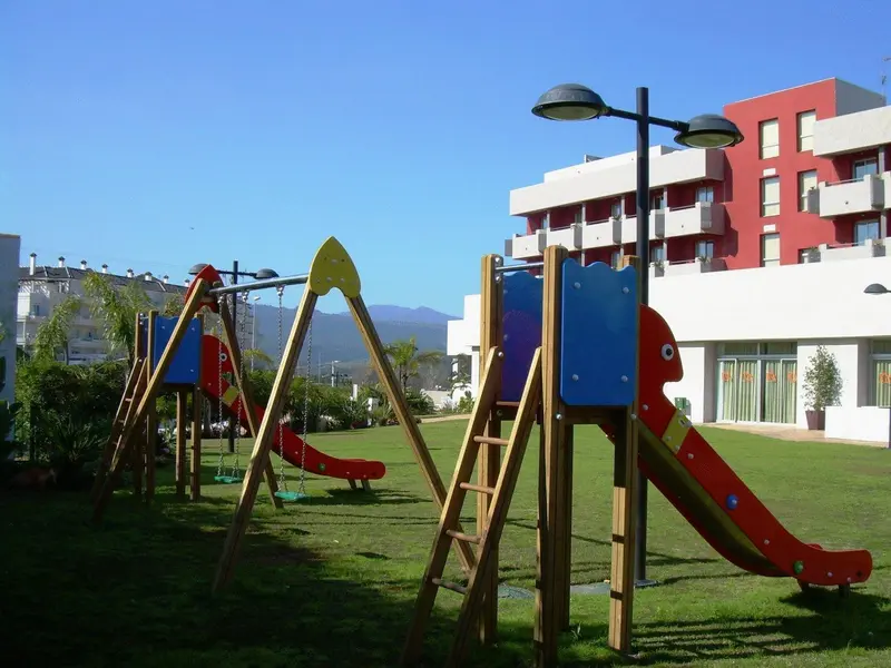 Aire de jeux colorée avec des balançoires et un toboggan sur une pelouse verte.