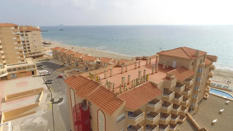 Vue aérienne d'un complexe hôtelier beige et orange avec des toits en tuiles rouges, situé en bord de mer.