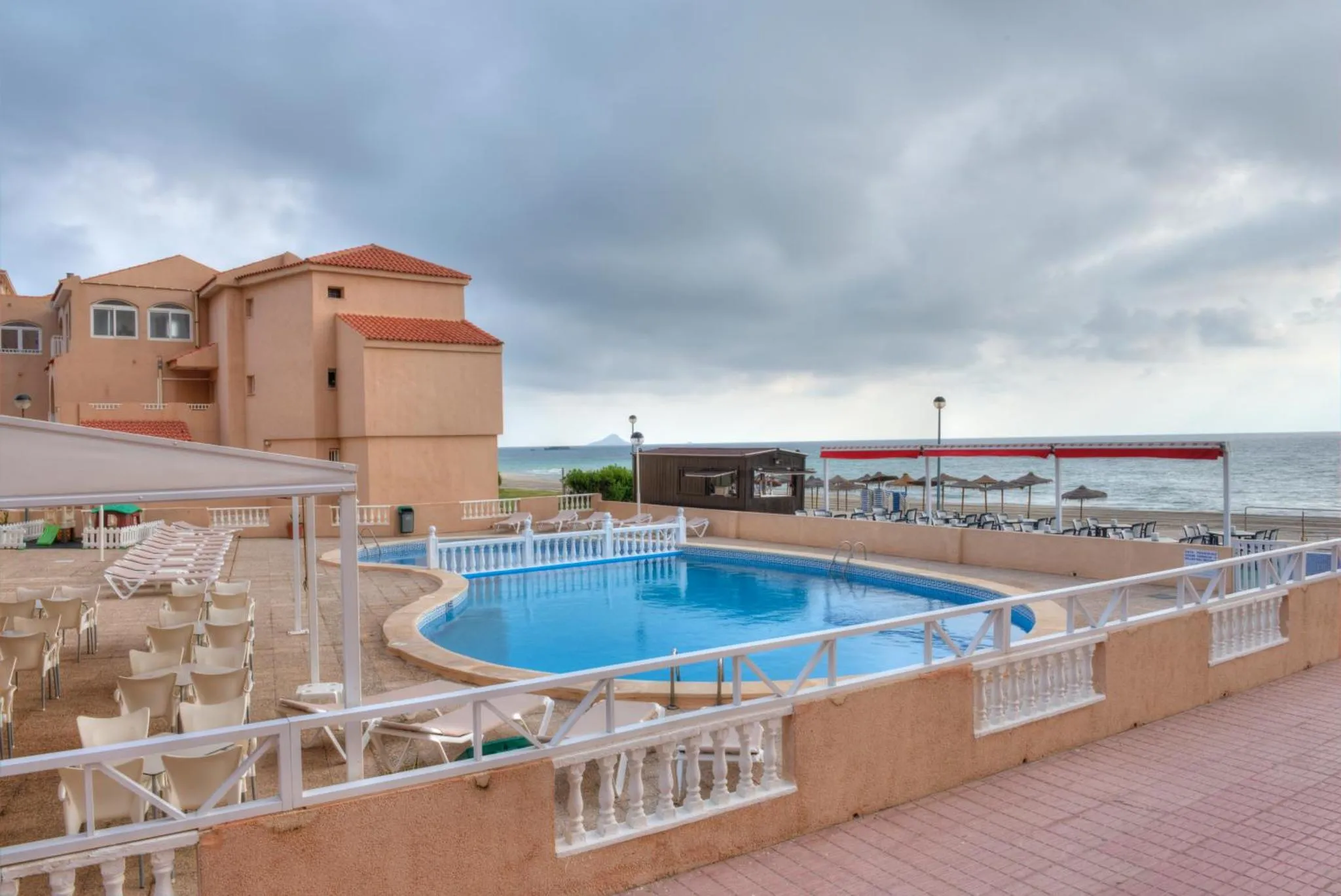 Une piscine avec des transats et des parasols devant un bâtiment de couleur claire.