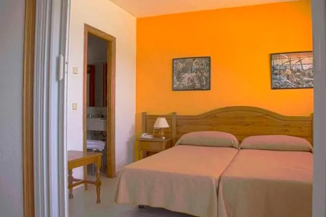 Une chambre avec deux lits simples et un mur orange décoré de tableaux.