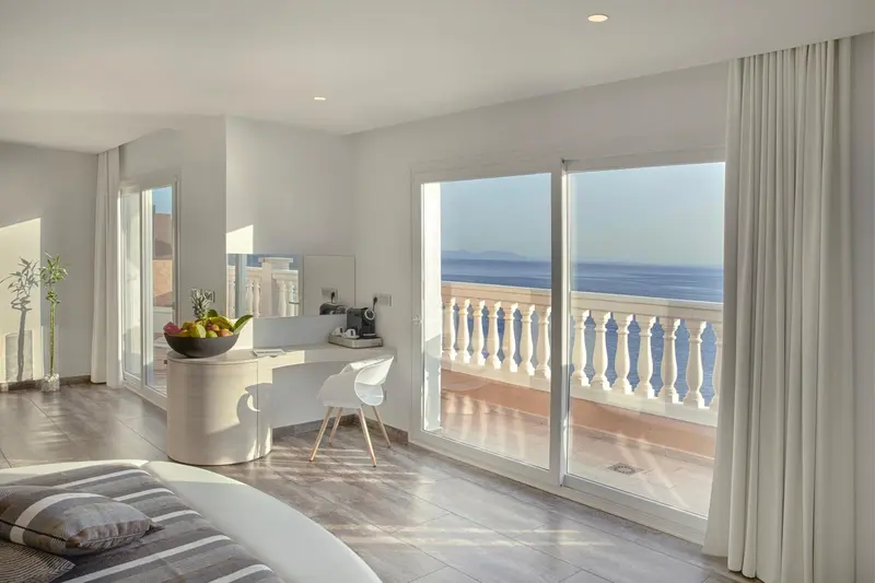Une chambre lumineuse avec un bureau et un balcon donnant sur la mer.