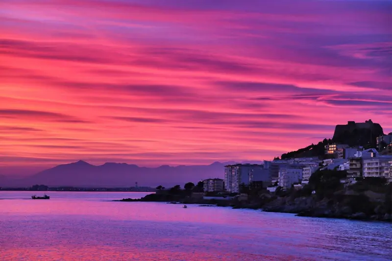 Ciel rose et orangé au-dessus d'une côte rocheuse et d'une ville.