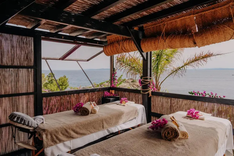 Deux tables de massage sont disposées dans un espace extérieur ombragé avec vue sur la mer.