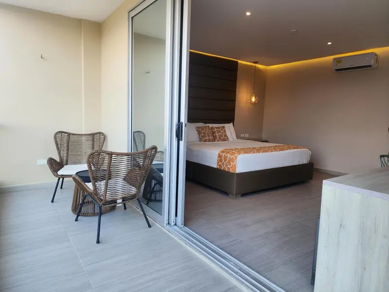 Une chambre lumineuse s'ouvre sur une terrasse avec des fauteuils en osier.