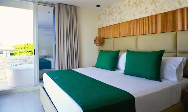 Une chambre lumineuse avec un grand lit recouvert d'une courtepointe verte et de coussins assortis.