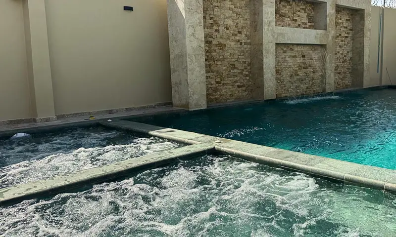 Une piscine avec un espace jacuzzi intégré et une cascade décorative en pierre.