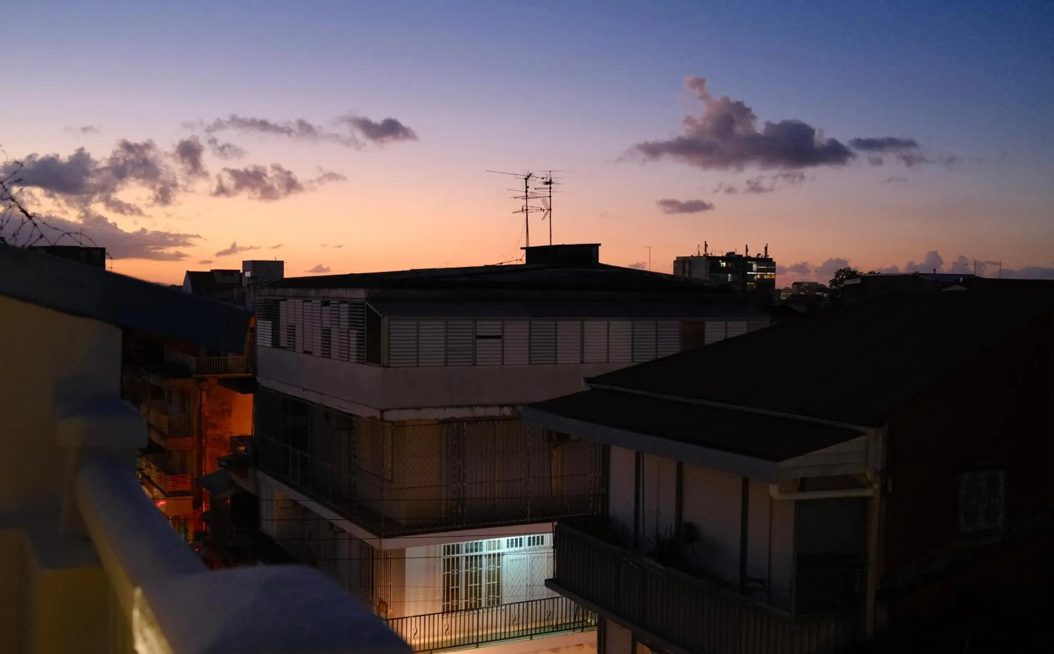 Toits d'immeubles au crépuscule avec un ciel orangé et nuageux.