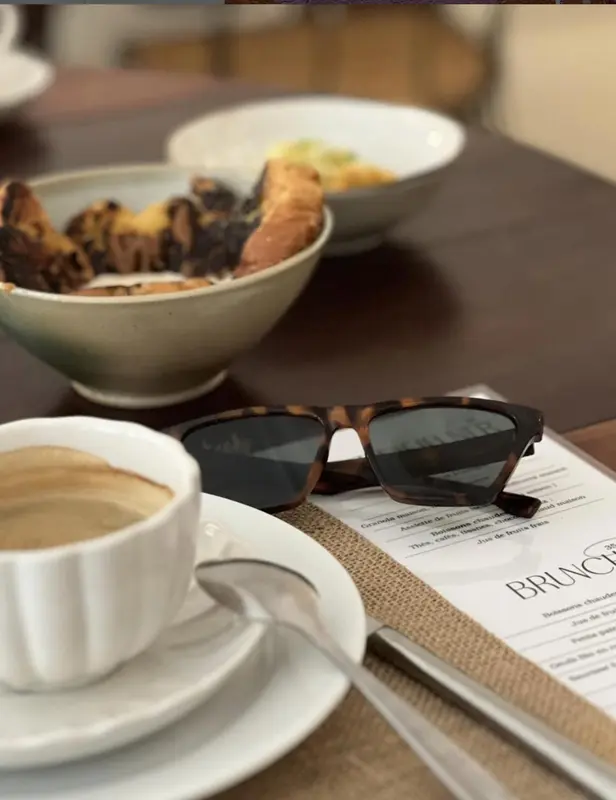 Une tasse de café et une assiette de viennoiseries sont posées sur une table avec des lunettes de soleil.