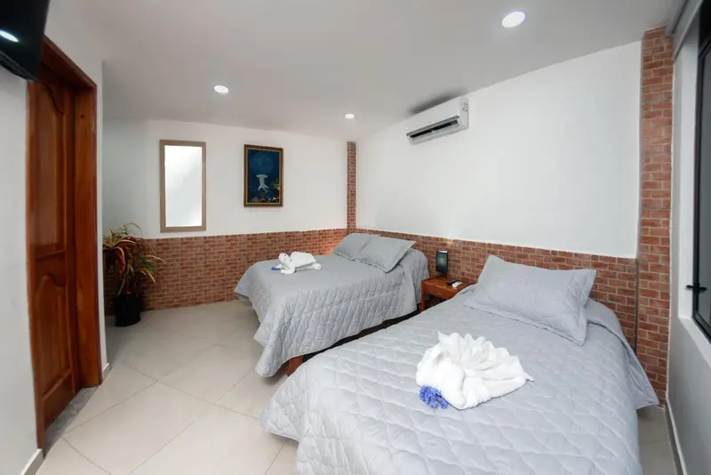 Chambre lumineuse avec deux lits simples et un mur en briques apparentes.