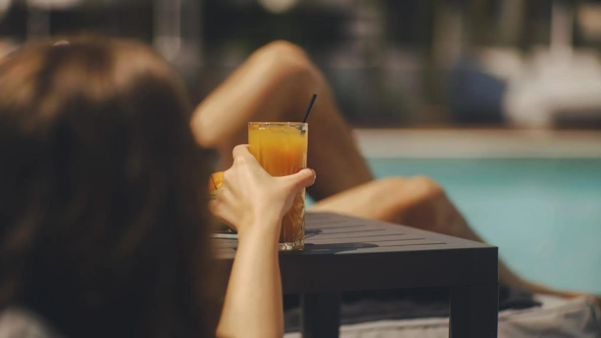 Une personne se détend au bord d'une piscine avec un verre.
