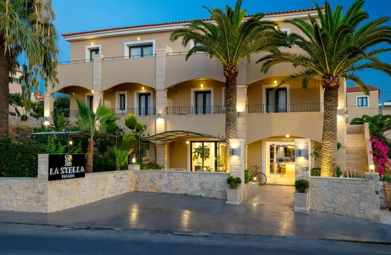 Façade d'un bâtiment beige à deux étages avec des palmiers et une entrée illuminée.