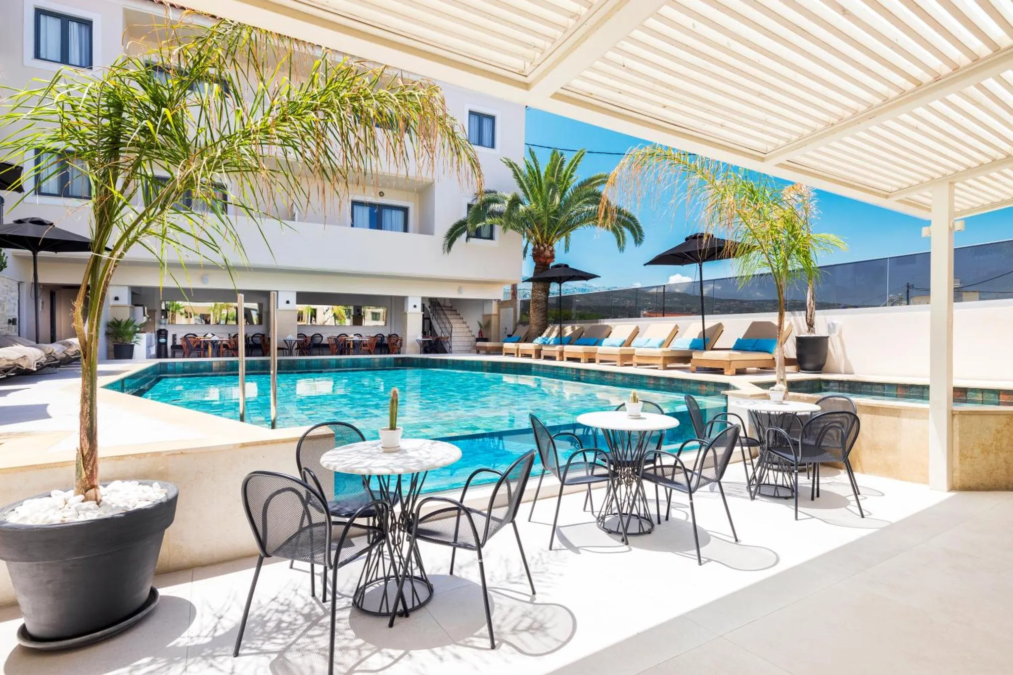 Terrasse ombragée avec tables et chaises près d'une piscine.