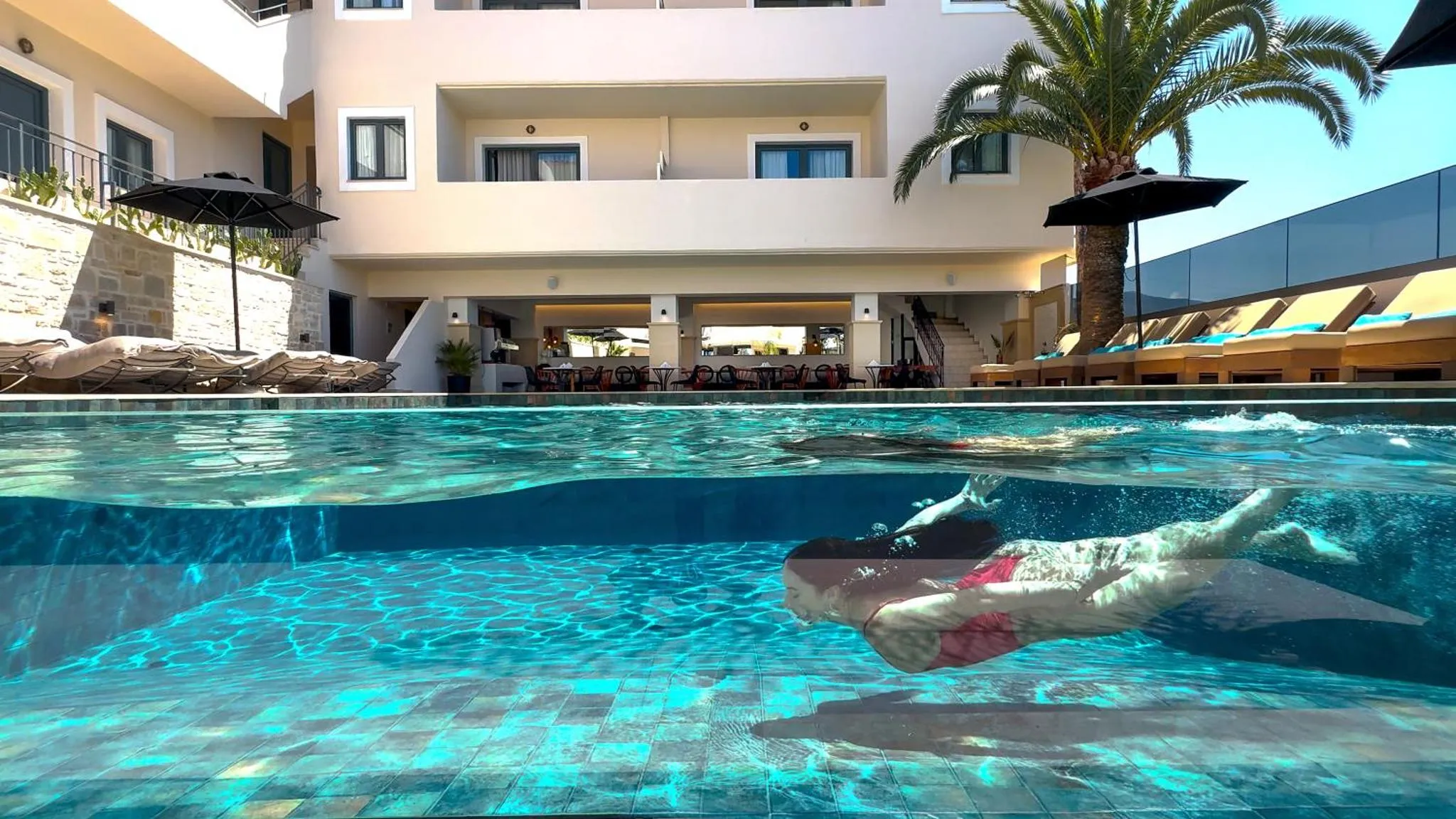 Une personne nage dans une piscine avec une vue sur un bâtiment et des transats.