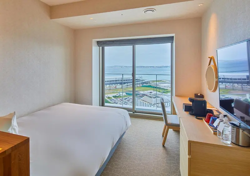 Chambre lumineuse avec un lit simple et une vue sur la mer.