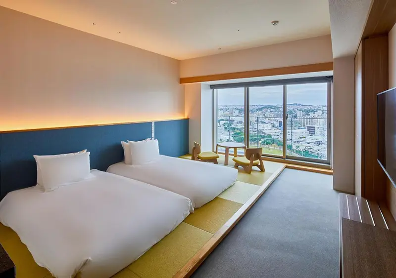 Chambre lumineuse avec lits jumeaux et vue sur la ville.