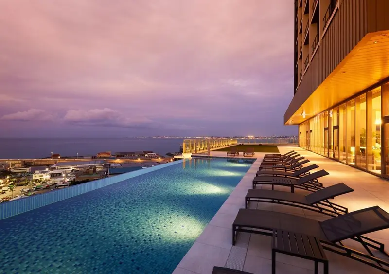 Une piscine à débordement illuminée surplombe la mer au coucher du soleil.