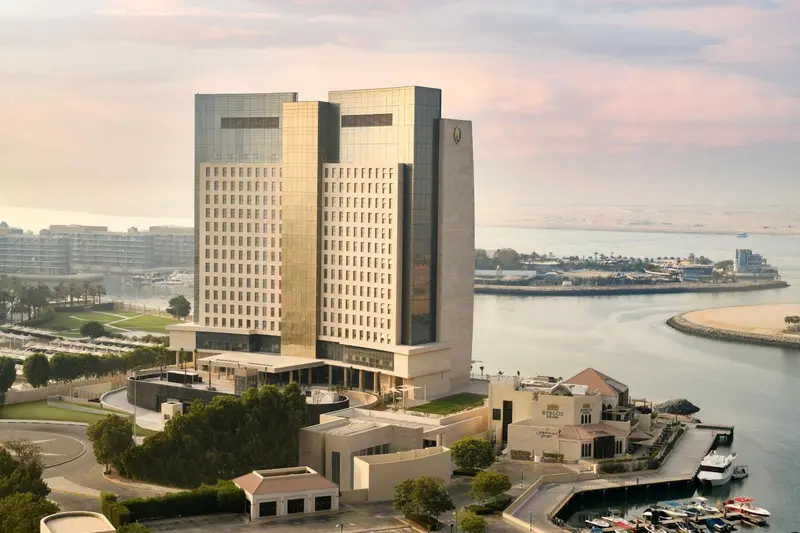Vue aérienne d'un grand bâtiment moderne au bord de l'eau, avec des bateaux amarrés au premier plan.