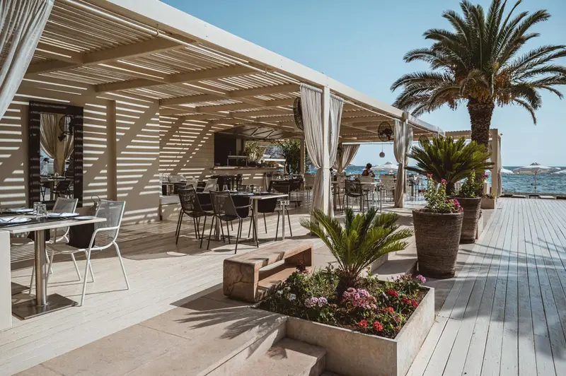 Terrasse ombragée avec tables et chaises près de la mer.
