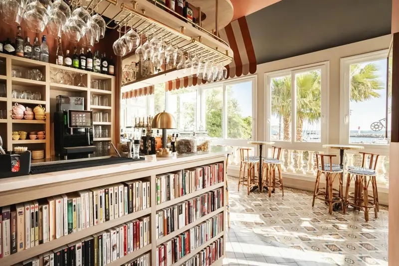Un bar lumineux avec un comptoir bien garni et des tabourets, donnant sur une vue extérieure.