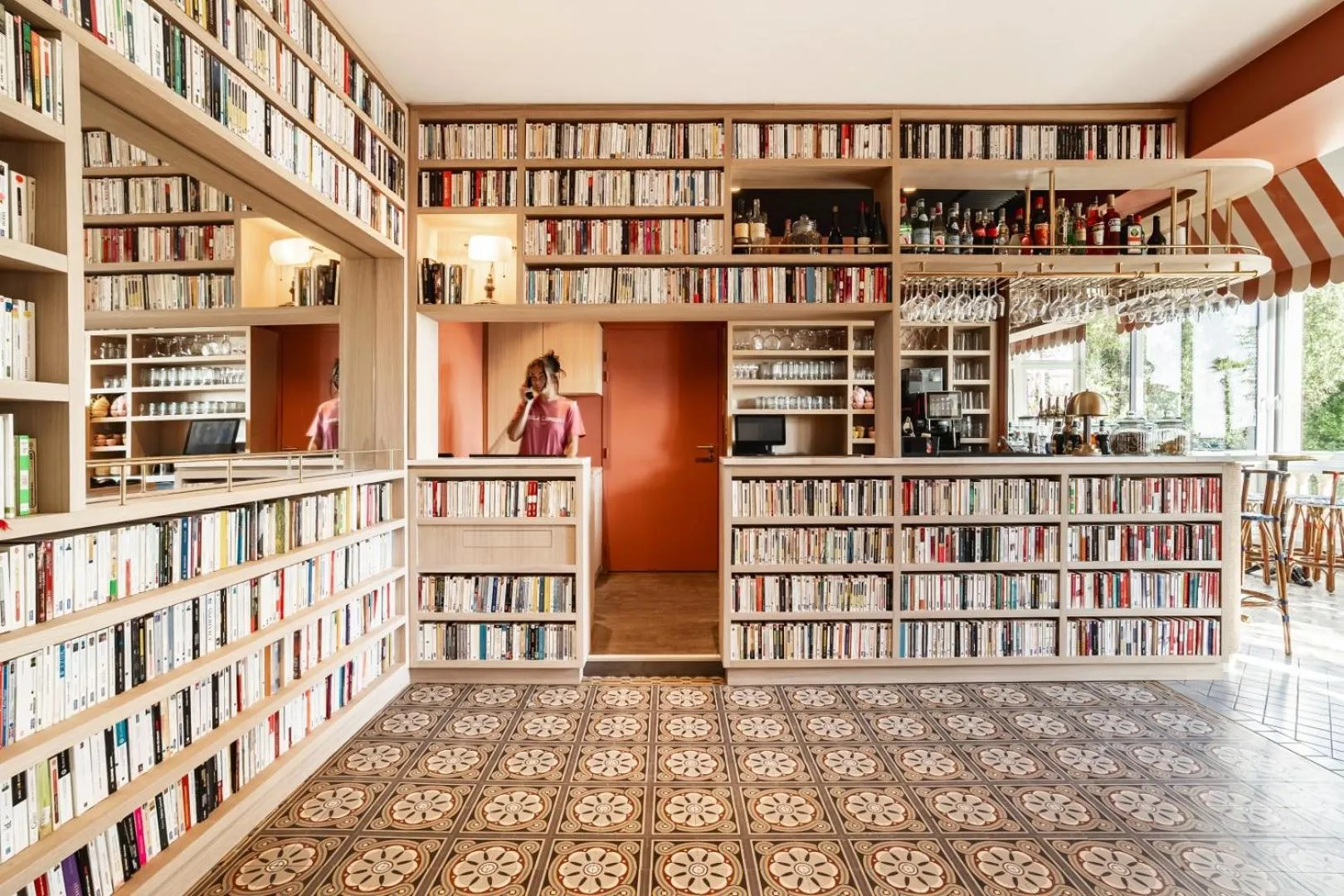 Une personne se tient derrière un comptoir dans une pièce décorée de nombreuses étagères à livres.