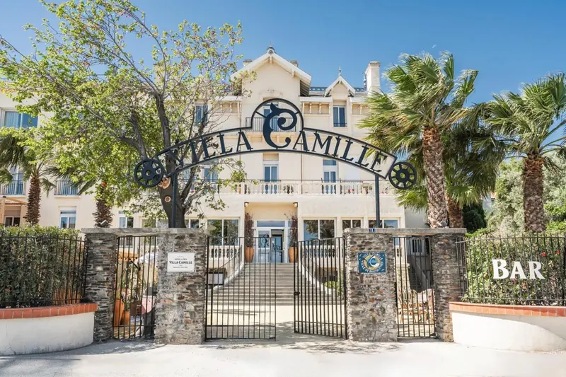 Façade d'un bâtiment blanc avec une arche ornée et des palmiers.