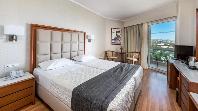 Chambre lumineuse avec un grand lit et une vue sur l'extérieur.