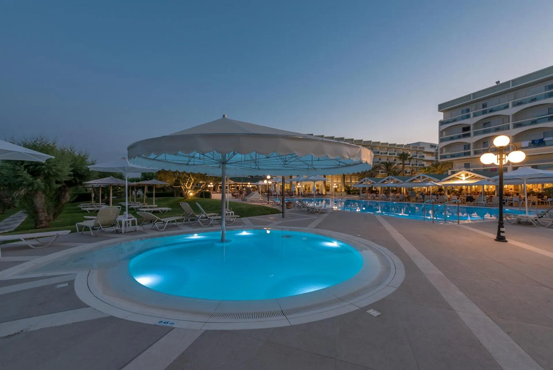 Une piscine illuminée avec des transats et des parasols au crépuscule.