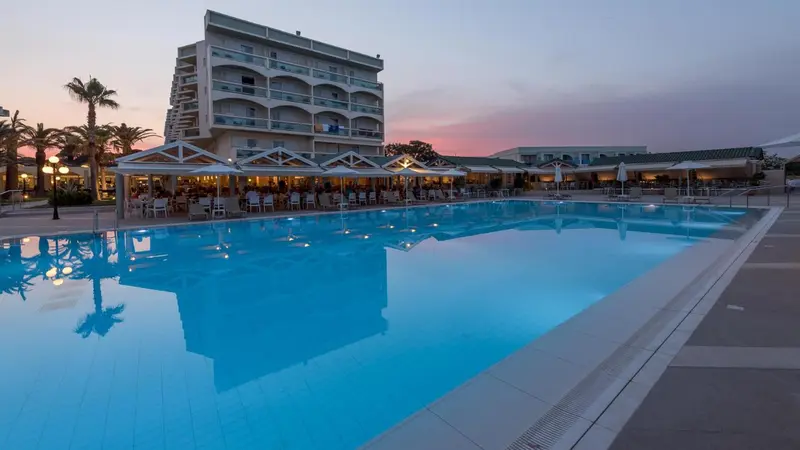 Une piscine rectangulaire reflète un bâtiment blanc et un ciel crépusculaire.