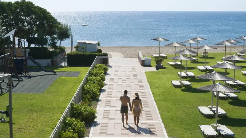 Une allée mène vers une plage avec des transats et des parasols.