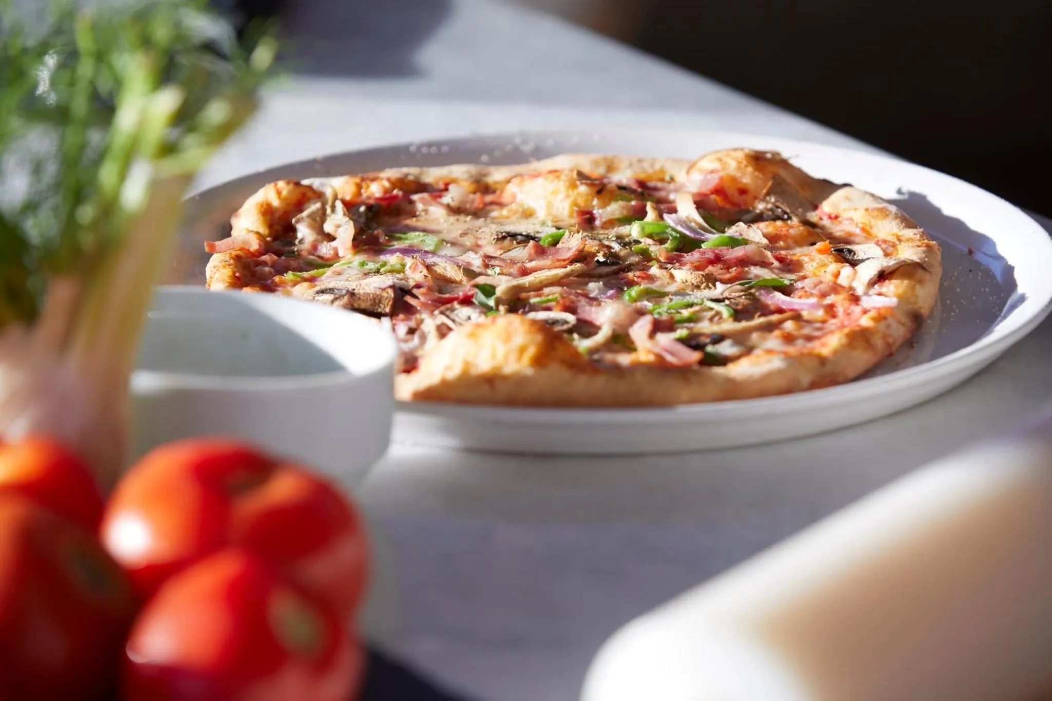 Une pizza garnie est présentée sur une assiette blanche avec des accompagnements.