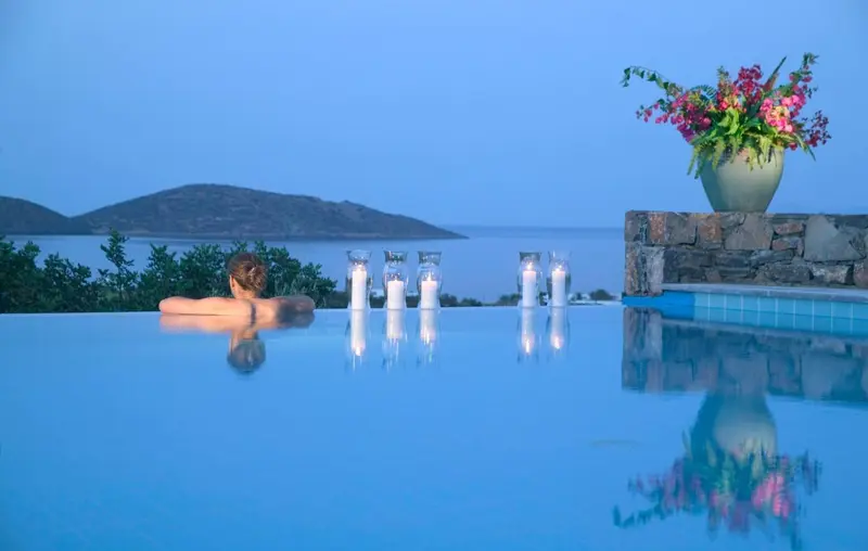 Une personne se détend dans une piscine à débordement avec vue sur la mer au coucher du soleil.