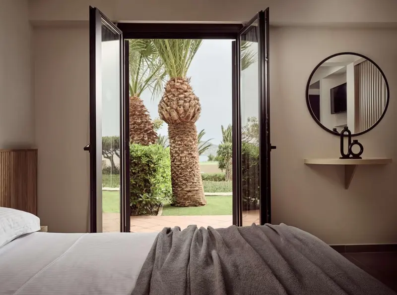 Une chambre s'ouvre sur une vue verdoyante avec des palmiers.