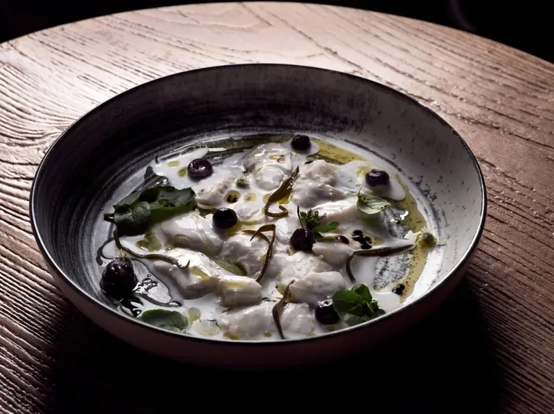 Assiette de poisson blanc cru, nappé d'une sauce claire et agrémenté d'olives et de verdure.