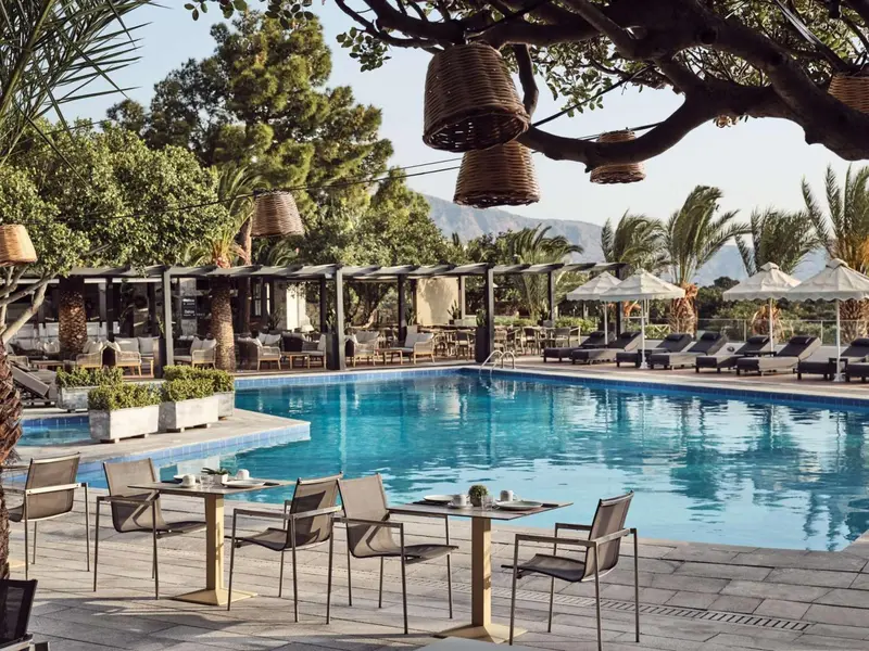 Une piscine bordée de chaises longues et de tables à manger sous des parasols.