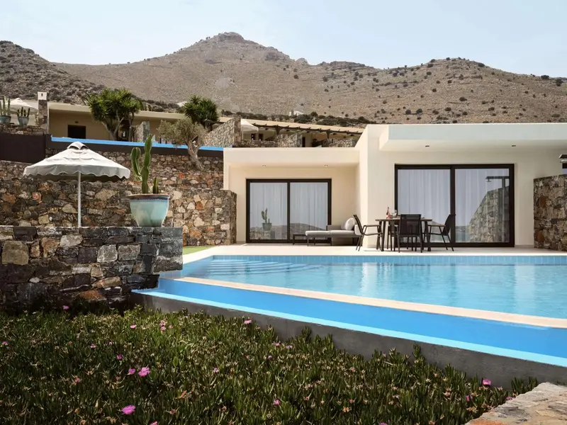Une piscine rectangulaire bordée de végétation et de fleurs devant un bâtiment blanc.