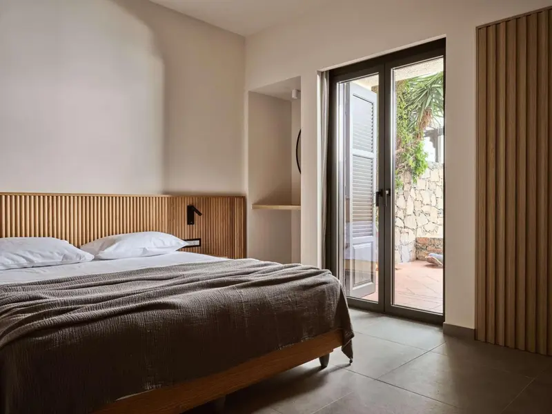 Une chambre lumineuse avec un grand lit et une porte-fenêtre donnant sur une cour.
